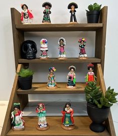 an assortment of mexican figurines on display in a wooden shelf with succulents and cacti