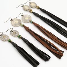 five pairs of tasseled earrings with beads and leather cord hang from hooks on a white surface