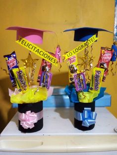 two vases with candy and graduation hats on top of a table in front of a yellow wall