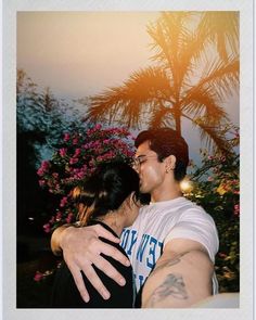 a man and woman embracing each other in front of flowers