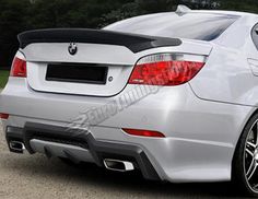 the rear end of a silver car parked in a parking lot with trees behind it