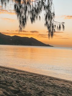 the sun is setting over the water and there is a bench on the beach next to it