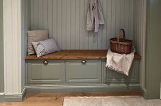 a wooden bench sitting in the middle of a room next to a basket and coat rack