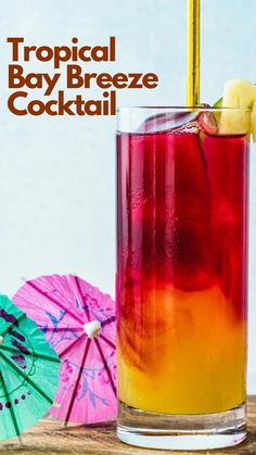 a colorful cocktail in a tall glass next to two umbrellas