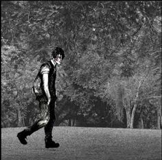 black and white photograph of a man walking in the grass with trees behind him on a sunny day