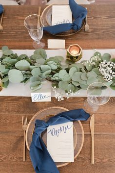 the table is set with blue napkins and greenery, silverware, and place settings