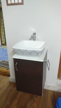 a white sink sitting on top of a wooden cabinet next to a blue trash can