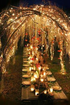 a long table with candles and lights under an arch made out of wood planks