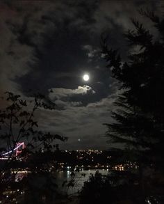 the full moon is shining brightly in the night sky over some water and trees with lights on them