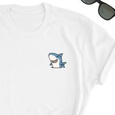 We have express delivery for our shirts! 📦⚡.  From cart to door in just 2-3 days, only for 3.5 USD extra.  You can find the express delivery option in the cart. Shark Shirt, Ocean Lover Tee Shirt, Shark Tee Top, Sharks Lover T-Shirt, Fun Shark Gift Shirt, Cute Sharks Lover Friends UNISEX Shirt Gift Friends will love it! This t-shirt feels soft and lightweight, with the right amount of stretch. It's comfortable and flattering for both men and women.  * 100% cotton (heather colors contain polyester) * Fabric weight: 5 oz  * Shoulder-to-shoulder taping * Side-seamed Time for Delivery: * Processing & production time is 1-6 business days (usually 2-3 days). * U.S. Shipping time: 3-5 business days.  * International shipping time: 4-15 days. - Please note European customers: Some orders going to White Crew Neck T-shirt With Cartoon Print, Funny White Short Sleeve Top, Funny White Shirt With Cartoon Print, Funny White Crew Neck Shirt, Cute White Crew Neck Shirt, White Shirt With Funny Print, White Funny Print Short Sleeve T-shirt, Funny White Print Crew Neck T-shirt, White T-shirt With Funny Print