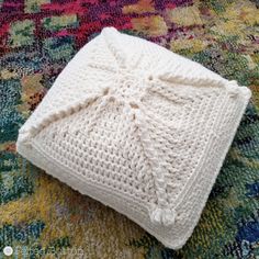 a white knitted pillow sitting on top of a rug