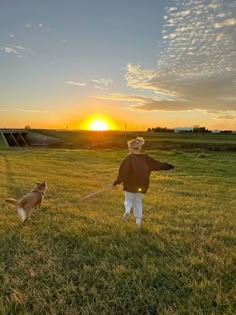 a man is walking his dog on a leash in the grass at sunset or dawn