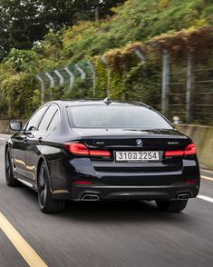 the rear end of a black bmw sedan driving on a road with trees in the background