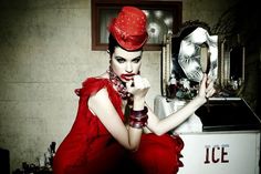 a woman in a red dress and hat sitting on a washing machine with her hand under her chin