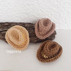 three crocheted hats sitting on top of a piece of driftwood next to a white wall