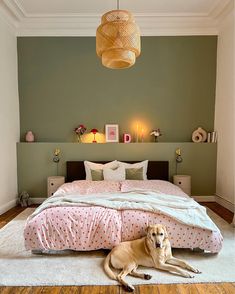 a dog laying on the floor in front of a bed with pink and white sheets