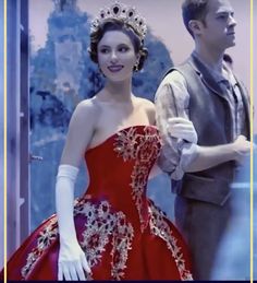 a man standing next to a woman wearing a red dress and tiara in front of a mirror