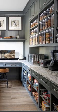 an organized kitchen with gray cabinets and wood flooring is pictured in this image, there are many items on the shelves