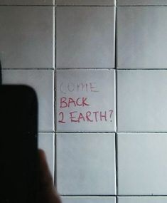 someone is writing on the wall next to a cell phone that reads come back 2 earth?