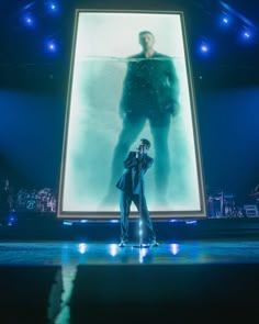 two people standing on stage in front of a large screen with the image of a man