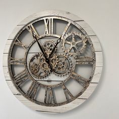 a clock made out of metal and wood with gears on the face is hanging on a wall