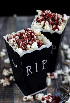 two black boxes filled with popcorn sitting on top of a wooden table covered in white and red sprinkles