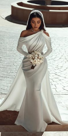 a woman in a white wedding dress standing on a stone walkway with her hands on her hips