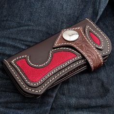 a red and brown leather wallet sitting on top of blue jeans