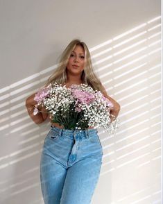 a woman standing in front of a white wall holding a bouquet of pink and white flowers