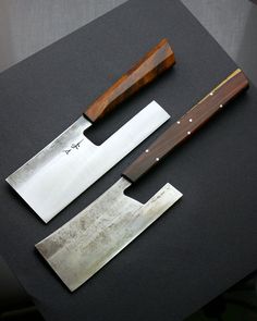 two knives are sitting next to each other on a black surface with a wooden handle