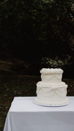 a wedding cake sitting on top of a white tablecloth covered table with trees in the background