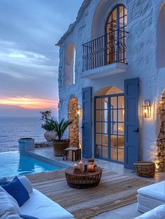 an outdoor living area with couches and tables next to the pool at dusk, overlooking the ocean