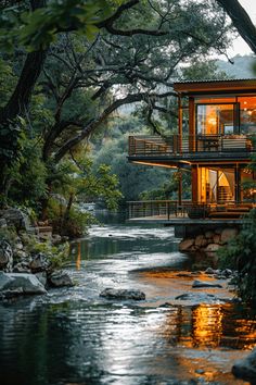 a house sitting on top of a lush green hillside next to a river in the forest