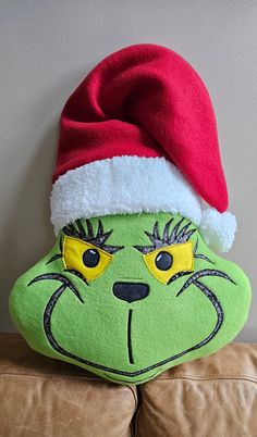 a green grin face pillow with a red santa hat on it's head sitting on a couch