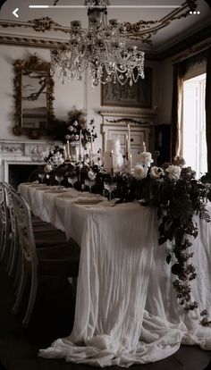 a dining room table with white cloths and flowers on it, surrounded by chandeliers