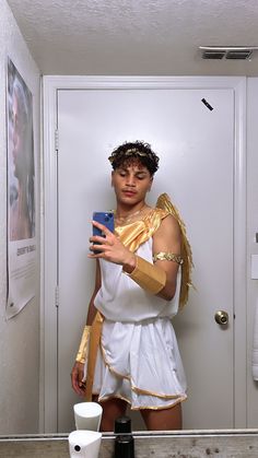 a woman dressed in white and gold taking a selfie with her cell phone while standing in front of a mirror