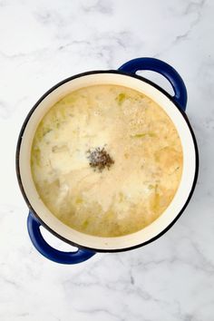 a pot filled with soup sitting on top of a white marble counter next to a blue handle