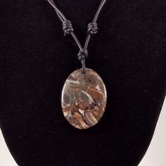 The Petrified Wood pendant is approximately 1.4 inches in length on natural black polished round leather. The necklace is adjustable from 16 inches to 32 inches by sliding the knots. The Titea singularis petrified wood in this cabochon is from the Triassic found in Madagascar. Petrified wood is fossilized remains of terrestrial vegetation. It is the result of a tree or tree-like plants having completely transitioned to stone by the process of permineralization. All the organic materials have bee Brown Necklace With Sliding Knot For Gift, Earthy Adjustable Round Necklace, Artisan Adjustable Necklace With Oval Pendant, Earthy Adjustable Round Pendant Necklace, Rustic Adjustable Round Pendant Necklaces, Adjustable Rustic Necklace With Round Pendant, Rustic Adjustable Necklace With Waxed Cord, Adjustable Rustic Necklace With Waxed Cord, Nature-inspired Necklace With Large Adjustable Pendant