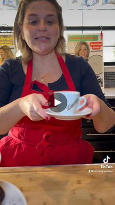 a woman in an apron is holding a cup and saucer while sitting at a table