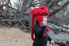 a young child wearing a red knitted dragon hat and holding a cell phone to her ear