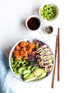 a white bowl filled with vegetables next to chopsticks and bowls of dipping sauce