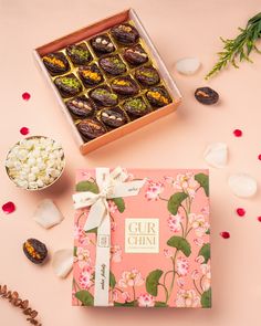 a box of chocolates next to some candies and flowers on a pink background