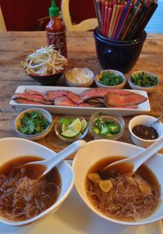 two bowls of soup with chopsticks on a table next to other dishes and utensils