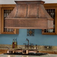 a large copper range hood in the middle of a kitchen with blue walls and wooden cabinets