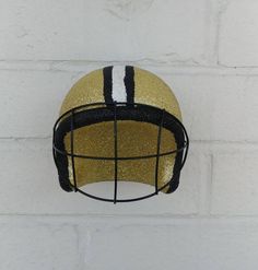 a football helmet hanging from the side of a brick wall with black and gold stripes