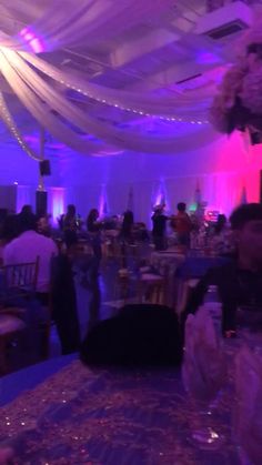 a banquet hall with purple lighting and white draping on the ceiling is filled with people