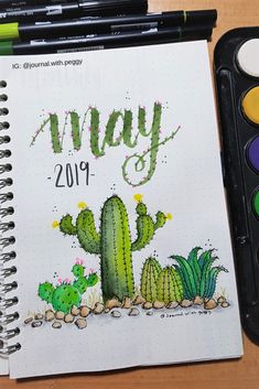 a notebook with the word may written on it next to watercolor paints and a cactus