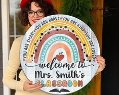 a woman holding up a welcome to mrs smith classroom sign