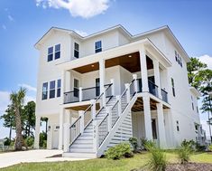 a white two story house with stairs leading to the second floor and third story balcony