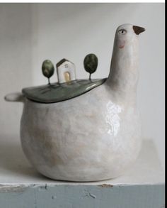 a white ceramic bird with three pins in it's beak sitting on top of a shelf